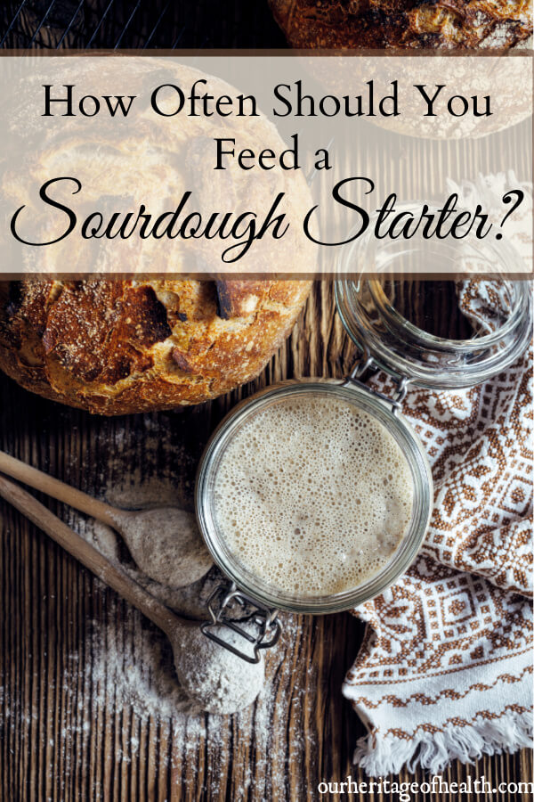 Jar of sourdough starter on table with loaf of bread and baking utensils